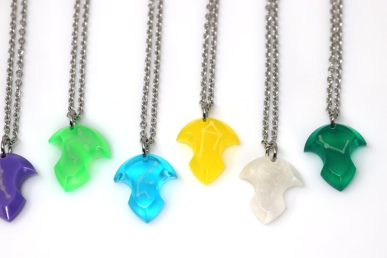 Puede incluir: Seis collares de plata con colgantes de diferentes colores. Cada colgante tiene forma de l&aacute;grima y presenta un dise&ntilde;o de constelaci&oacute;n. Los colgantes son morados, verdes, azules, amarillos, blancos y verdes.