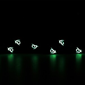May include: A black background with multiple glowing green symbols scattered across the surface. The symbols are all the same and resemble a stylized eye.