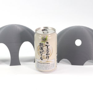 May include: Two gray 3D printed half-dome shapes with holes, one with two holes and the other with one hole, surrounding a can of Japanese beer labeled "Ichi-go Ichi-e" with Japanese text.