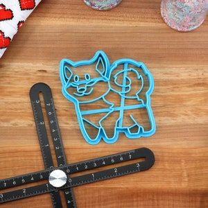 May include: A blue plastic cookie cutter shaped like a cartoon dog. The cutter has a detailed outline of a dog with a tail curled around its body.