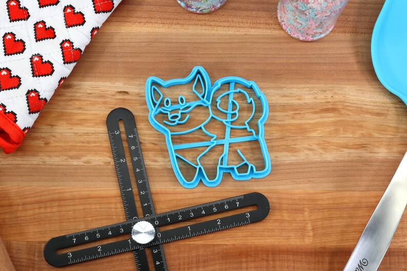 May include: A blue plastic cookie cutter shaped like a cartoon dog. The cutter has a detailed outline of a dog with a tail curled around its body.