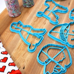 May include: A set of six blue plastic cookie cutters shaped like different dogs. The cutters are on a wooden surface.