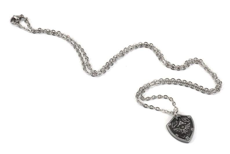 May include: A silver chain necklace with a pendant shaped like the Hylian Shield from the Legend of Zelda video game series.