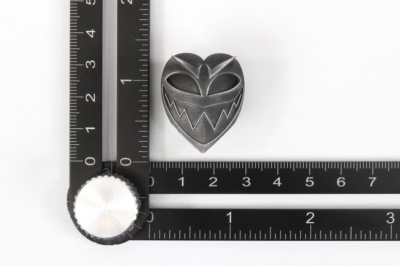 May include: A silver heart-shaped pin with a black and white grinning face design.