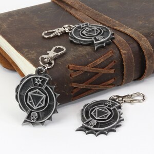 May include: Three silver metal keychains with a skull, a die, and a star design. The keychains are hanging from a brown leather journal.