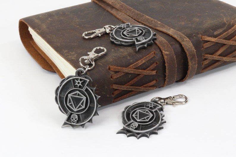 May include: Three silver metal keychains with a skull, a die, and a star design. The keychains are hanging from a brown leather journal.