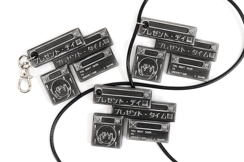 May include: Two black and silver necklaces with pendants featuring the Japanese text "プレゼント・デイ" and "プレゼント・タイム" along with a cartoon face. The necklaces are on a white background.