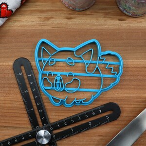 May include: Blue plastic cookie cutter shaped like a cartoon dog with a striped pattern. The cutter is on a wooden surface.
