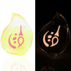 May include: A yellow glass teardrop pendant with a pink swirl design. The pendant glows in the dark.