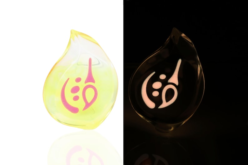 May include: A yellow glass teardrop pendant with a pink swirl design. The pendant glows in the dark.