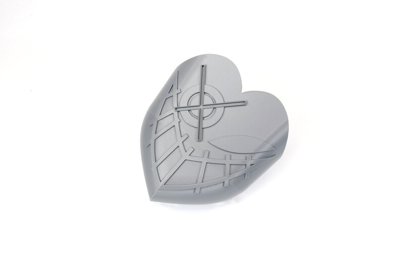 May include: A gray, heart-shaped object with a leaf-like design and a crosshair pattern. The object has a grid-like pattern and a curved edge, suggesting it may be a decorative item or a component of a larger design. The object is on a white background.