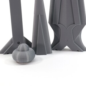 May include: Three gray 3D printed objects, two are tall and narrow, one is short and round. The tall objects have a pointed top and a wide base. The round object has a smooth, textured surface.