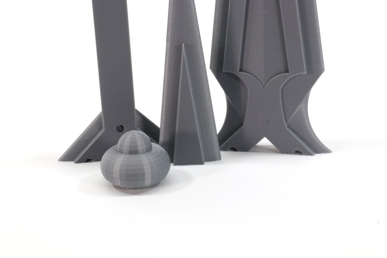 May include: Three gray 3D printed objects, two are tall and narrow, one is short and round. The tall objects have a pointed top and a wide base. The round object has a smooth, textured surface.