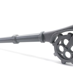 May include: A gray metal key with a long handle and a gear-shaped head. The handle is textured and the gear has four spokes.