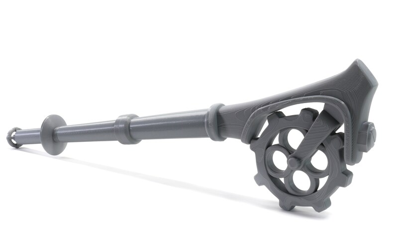 May include: A gray metal key with a long handle and a gear-shaped head. The handle is textured and the gear has four spokes.