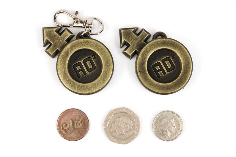 May include: Two gold-colored metal keychains with a black circle containing the text "AD^2" and a gold-colored arrow. Three coins are also shown in the image.