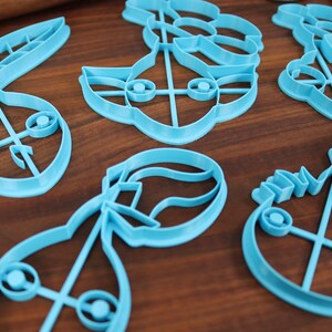 May include: A set of six blue plastic cookie cutters shaped like different characters. The cutters are on a wooden surface.