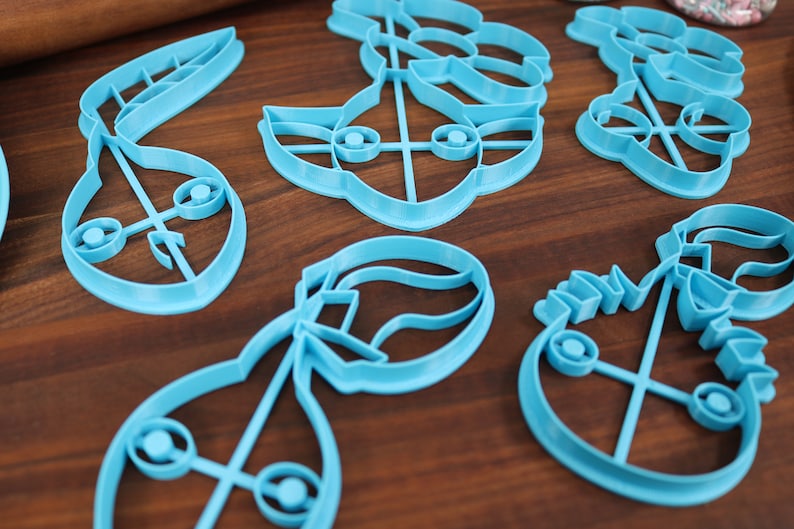 May include: A set of six blue plastic cookie cutters shaped like different characters. The cutters are on a wooden surface.