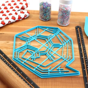 May include: A blue plastic snowflake cookie cutter on a wooden surface with a rolling pin, a ruler, a spatula, and two jars of sprinkles.
