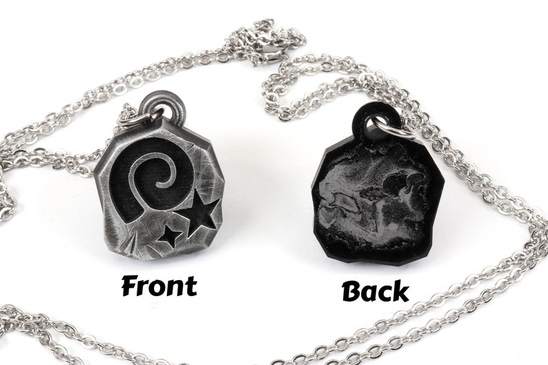May include: A silver necklace with a pendant featuring a spiral and two stars on the front and a textured design on the back.