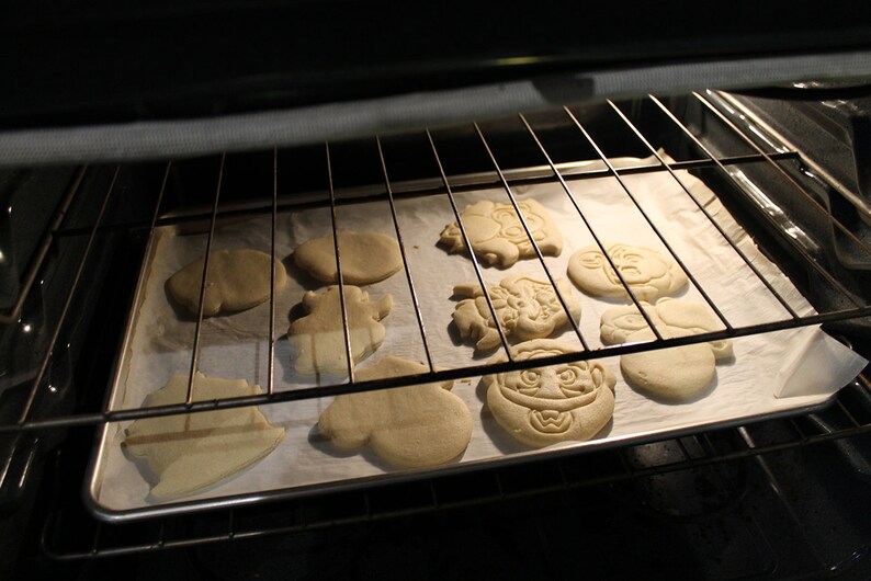 May include: A baking sheet with a variety of unbaked cookies in an oven. The cookies are shaped like different characters and are ready to be baked.
