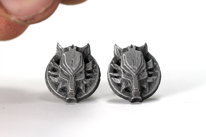 Op de afbeelding: Een paar zilverkleurige metalen oorbellen met een wolfskopontwerp. De wolfskop is omgeven door een cirkelvormig ontwerp met een getextureerd oppervlak.