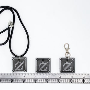 Pu&ograve; includere: Tre ciondoli color argento con un designo stilizzato della lettera Z. I ciondoli sono mostrati su una superficie bianca con un righello per la scala. Il ciondolo a sinistra &egrave; su un cordoncino nero, il ciondolo al centro &egrave; su una superficie bianca e il ciondolo a destra &egrave; su una catenina argentata.