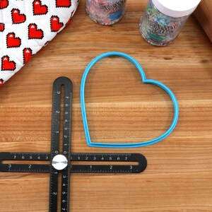 May include: A blue heart-shaped cookie cutter on a wooden surface with a black ruler and a rolling pin.