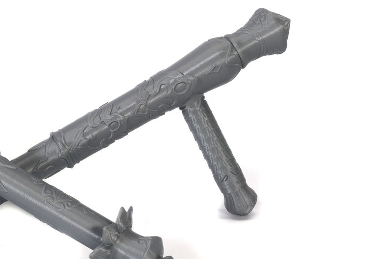 May include: A gray, intricately designed, metal weapon with a handle and a long, pointed blade. The weapon has a decorative pattern on the handle and blade.