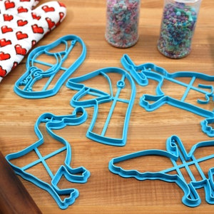 May include: A set of blue plastic cookie cutters shaped like a duck, a bird, a hat, a shoe, and a unicorn. The cutters are on a wooden surface.