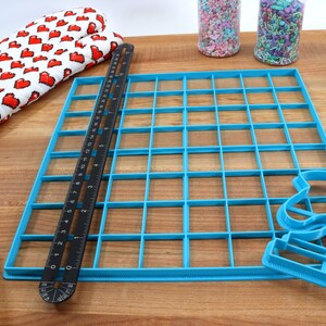 May include: A blue plastic grid with 36 squares, a black ruler, and a blue plastic cookie cutter shaped like a crescent moon.