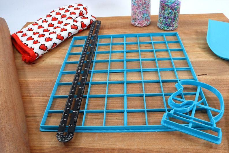 May include: A blue plastic grid with 36 squares, a black ruler, and a blue plastic cookie cutter shaped like a crescent moon.