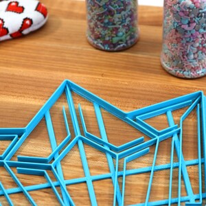 Puede incluir: Un cortador de galletas geom&eacute;trico de pl&aacute;stico azul en forma de estrella. El cortador est&aacute; sobre una superficie de madera.