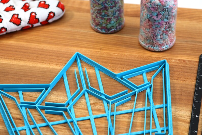 Puede incluir: Un cortador de galletas geom&eacute;trico de pl&aacute;stico azul en forma de estrella. El cortador est&aacute; sobre una superficie de madera.