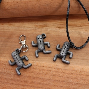 May include: Three silver-colored pendants shaped like a character from a video game, hanging on black cords. One pendant is attached to a silver key chain.