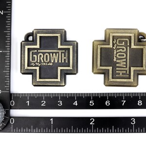 May include: Two gold-colored metal keychains shaped like crosses. One keychain has the word "GROWTH" in black lettering on a black background. The other keychain has the word "GROWTH" in gold lettering on a gold background. Both keychains have a silver metal ring.