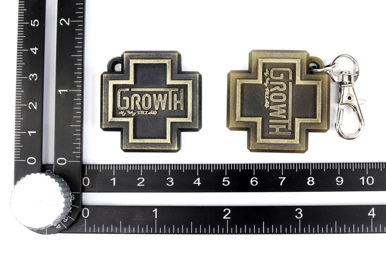 May include: Two gold-colored metal keychains shaped like crosses. One keychain has the word "GROWTH" in black lettering on a black background. The other keychain has the word "GROWTH" in gold lettering on a gold background. Both keychains have a silver metal ring.