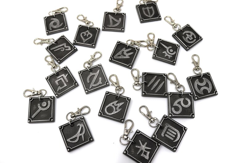 May include: A set of 18 silver-colored metal keychains with different symbols on each. The keychains are square-shaped and have a silver-colored metal ring.