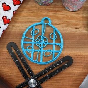 May include: A blue plastic cookie cutter shaped like a circle with a decorative design inside. The cutter is on a wooden surface with other baking tools.