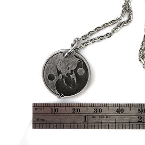May include: A silver necklace with a round pendant featuring a yin yang symbol with a dragon and a phoenix design. The pendant is approximately 2 cm in diameter.