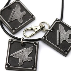 May include: Three silver metal pendants with a black background and an anvil design. The pendants are on a black cord and one is attached to a silver metal key chain.