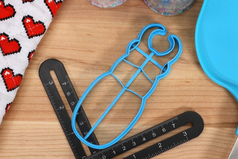 May include: A blue plastic cookie cutter shaped like a beetle. The cutter has a handle on the top and a detailed design.
