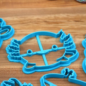 May include: A set of five blue plastic cookie cutters shaped like various animals. The cutters are on a wooden surface.