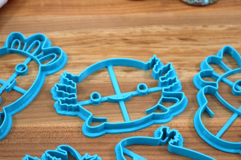 May include: A set of five blue plastic cookie cutters shaped like various animals. The cutters are on a wooden surface.