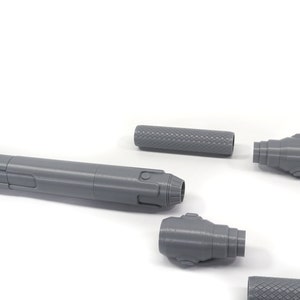 K&ouml;nnte beinhalten: Ein zerlegtes, graues 3D-gedrucktes Modell einer futuristischen Waffe. Die Waffe besteht aus f&uuml;nf Teilen: einem langen Lauf, zwei Endkappen und zwei k&uuml;rzeren Teilen.