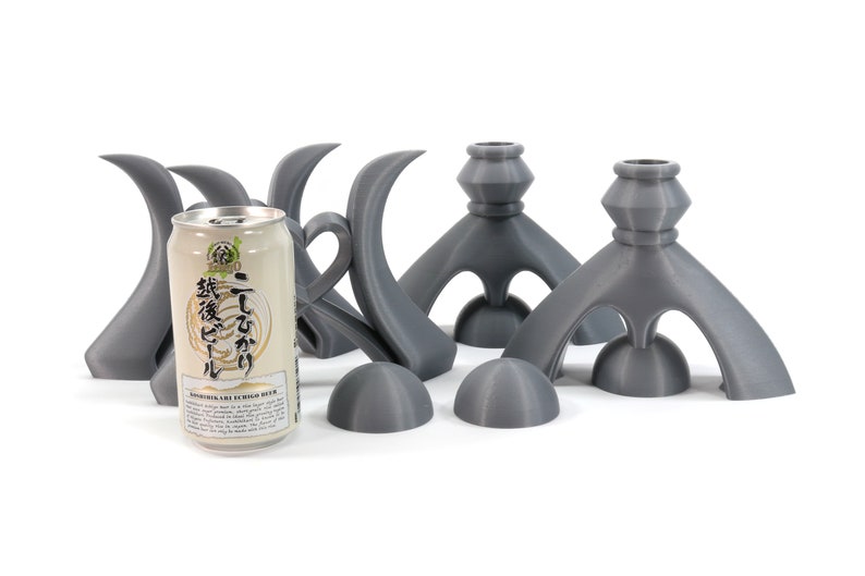 May include: Four gray ceramic candle holders with a unique, abstract design. The holders are shaped like a stylized bird with a rounded base and a tall, curved neck. A can of Japanese beer is in the center of the image.