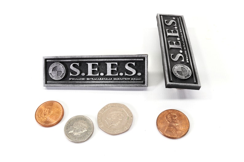 May include: Two silver metal rectangular badges with the text "S.E.E.S. SPECIALIZED EXTRACURRICULAR EXECUTION SQUAD" and a logo. The badges are on a white surface with four copper-colored coins.