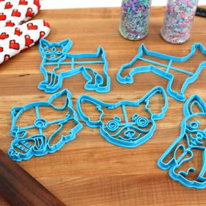 Puede incluir: Cinco cortadores de galletas de pl&aacute;stico azul con forma de perro chihuahua. Los cortadores est&aacute;n sobre una superficie de madera.