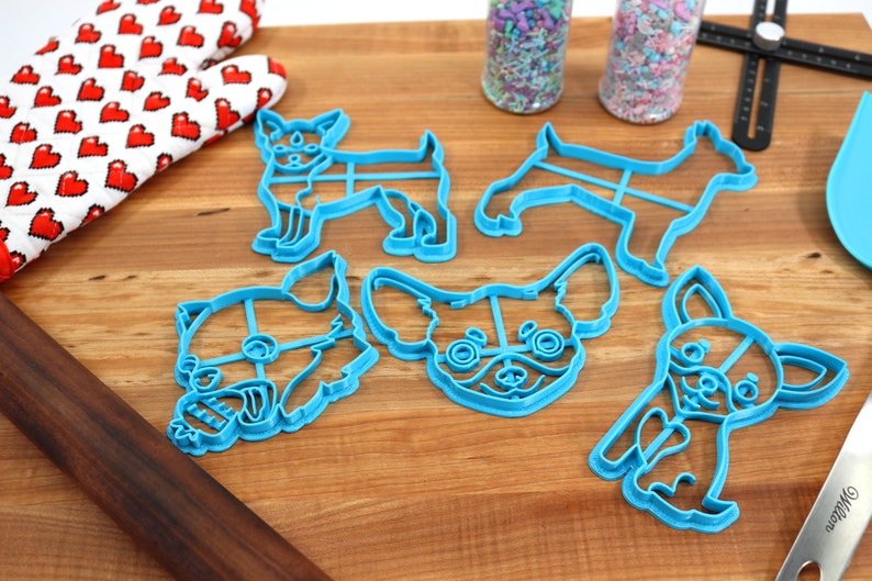 Puede incluir: Cinco cortadores de galletas de pl&aacute;stico azul con forma de perro chihuahua. Los cortadores est&aacute;n sobre una superficie de madera.