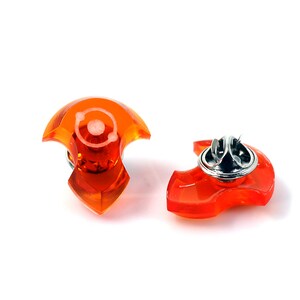 May include: Two orange plastic safety pins with a silver metal pin. The pins are shaped like a crescent moon.